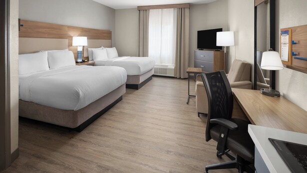 Habitación de hotel con dos camas, un escritorio, una silla, un televisor y una ventana con cortinas.