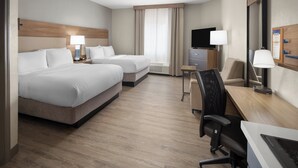 Habitación de hotel con dos camas, un escritorio, una silla, un televisor y una ventana con cortinas.
