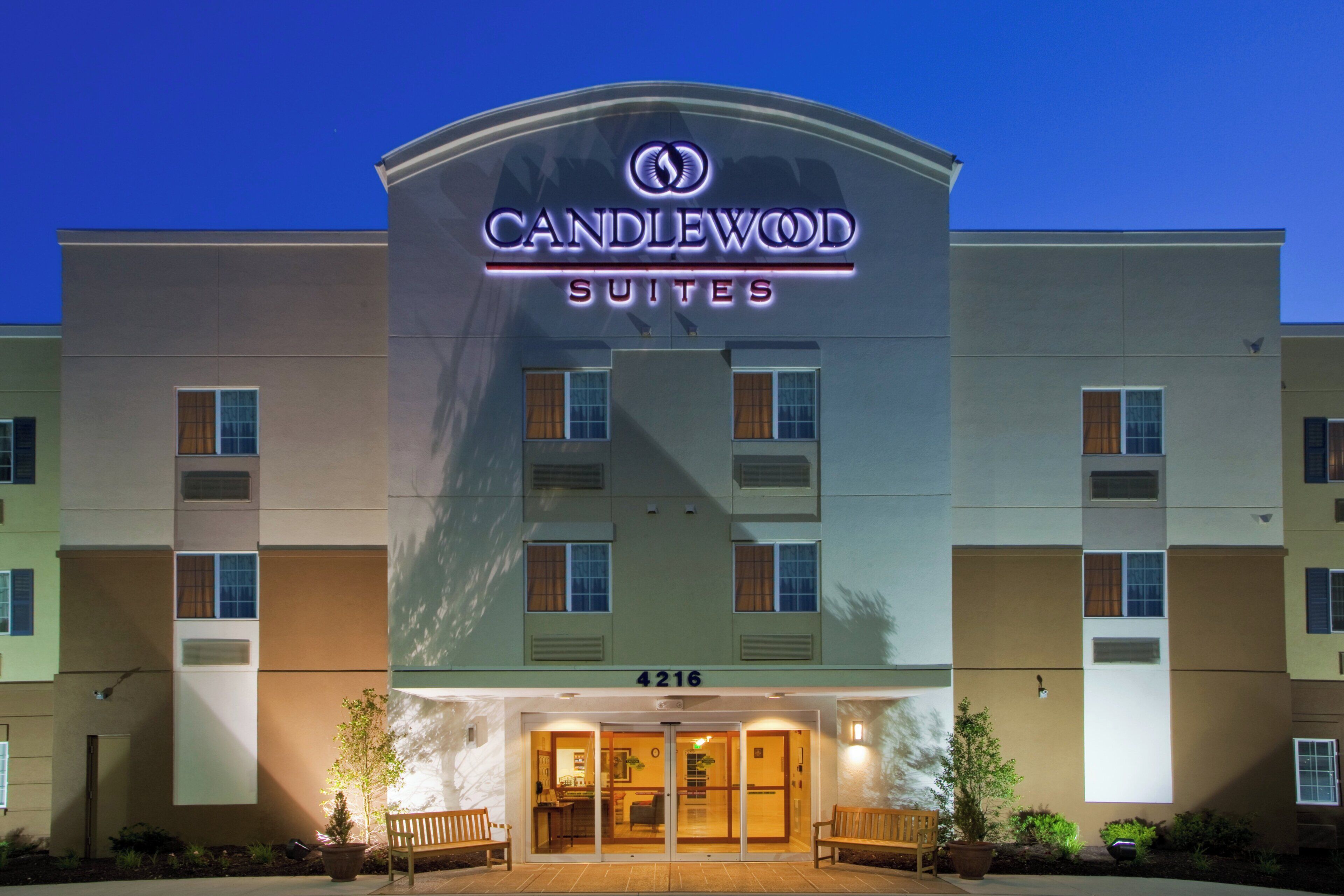 Un hotel con un llamativo letrero de 'CANDLEWOOD SUITES', una entrada a nivel de suelo y el número '4216' visible.