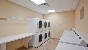 A laundry room with four stacked front-loading washers and dryers, a white bench, and a wall-mounted drying rack.