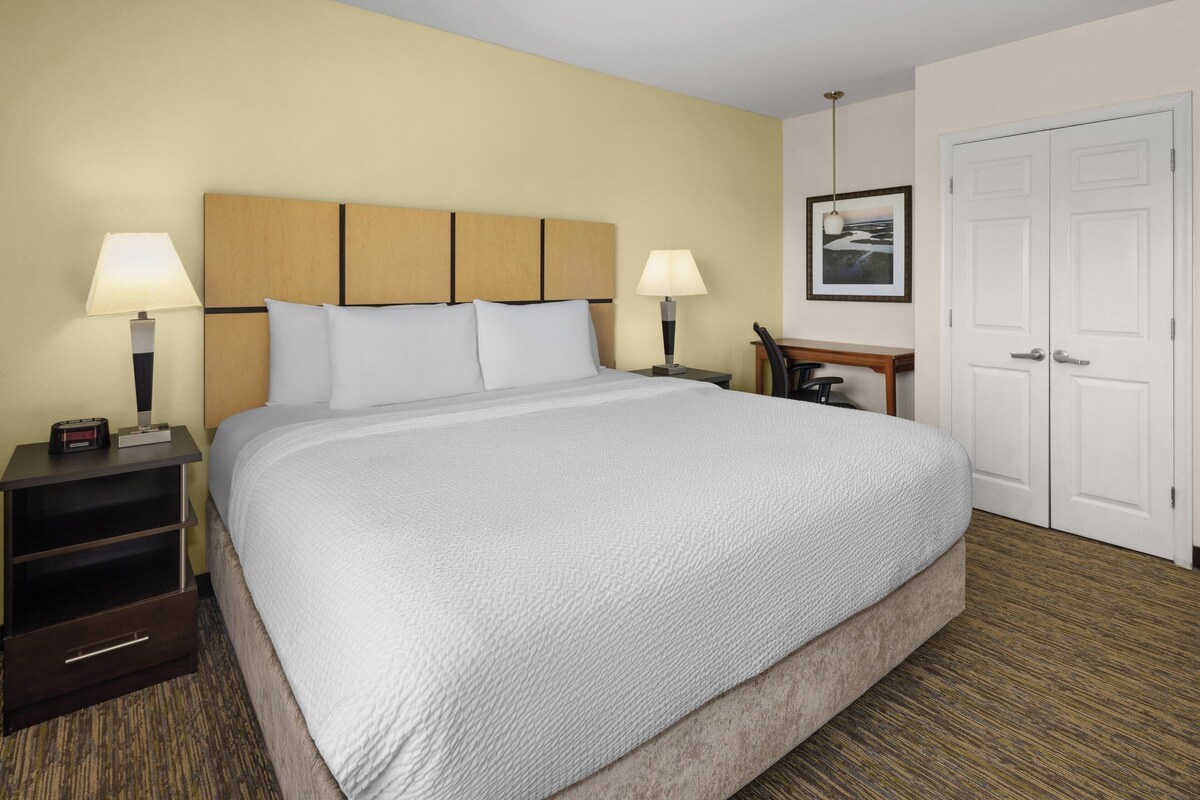 A hotel room with a large bed, two bedside tables with lamps, a desk, and a door.