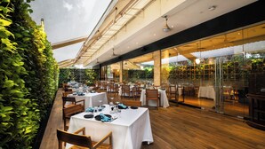 An indoor dining area with tables set for service, wooden flooring, and a glass wall with greenery. - Marriott Suites Pune (Pune)