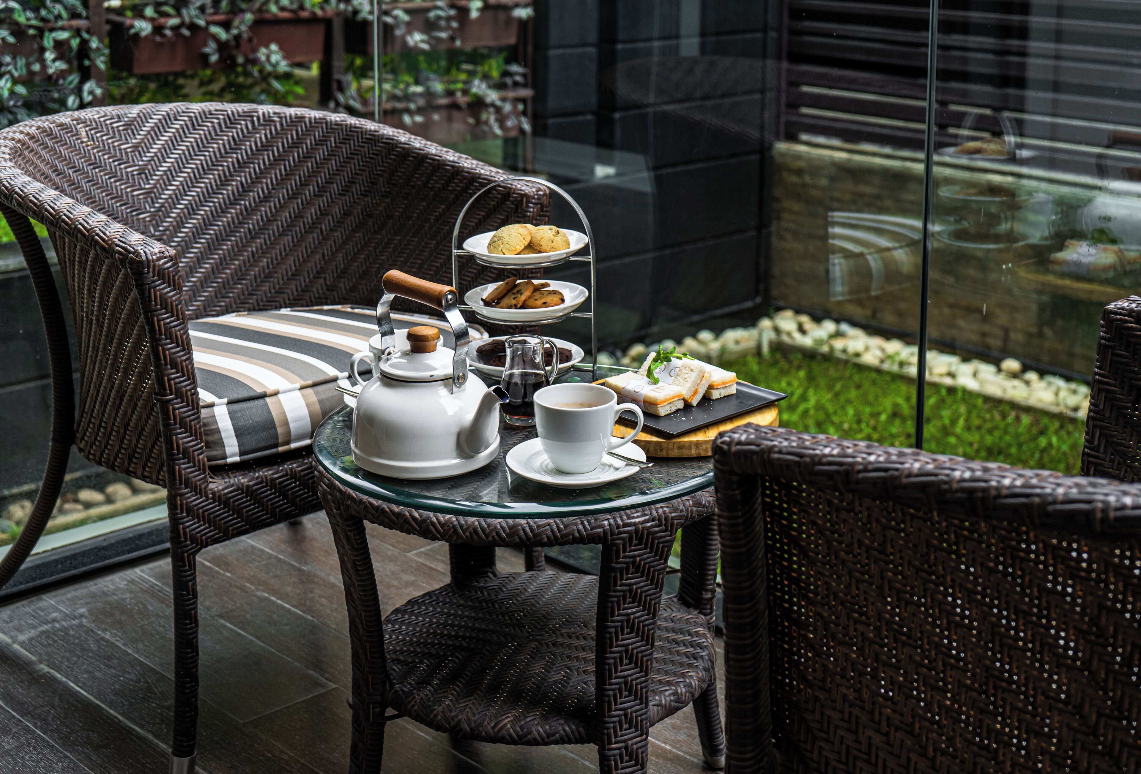 A wicker chair with a tray table holding a teapot, cup, and cookies.