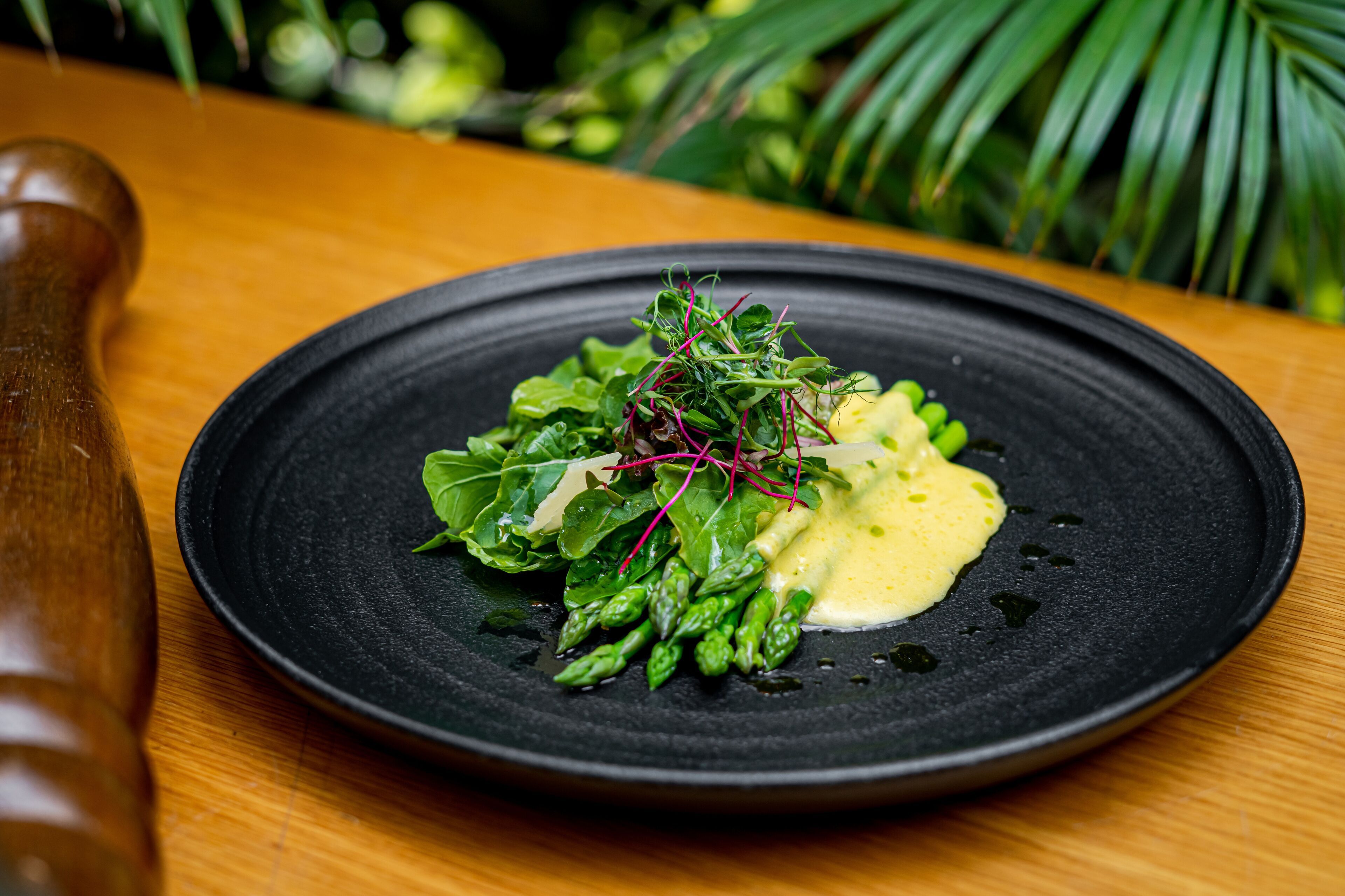 A black plate with a salad on a wooden table.