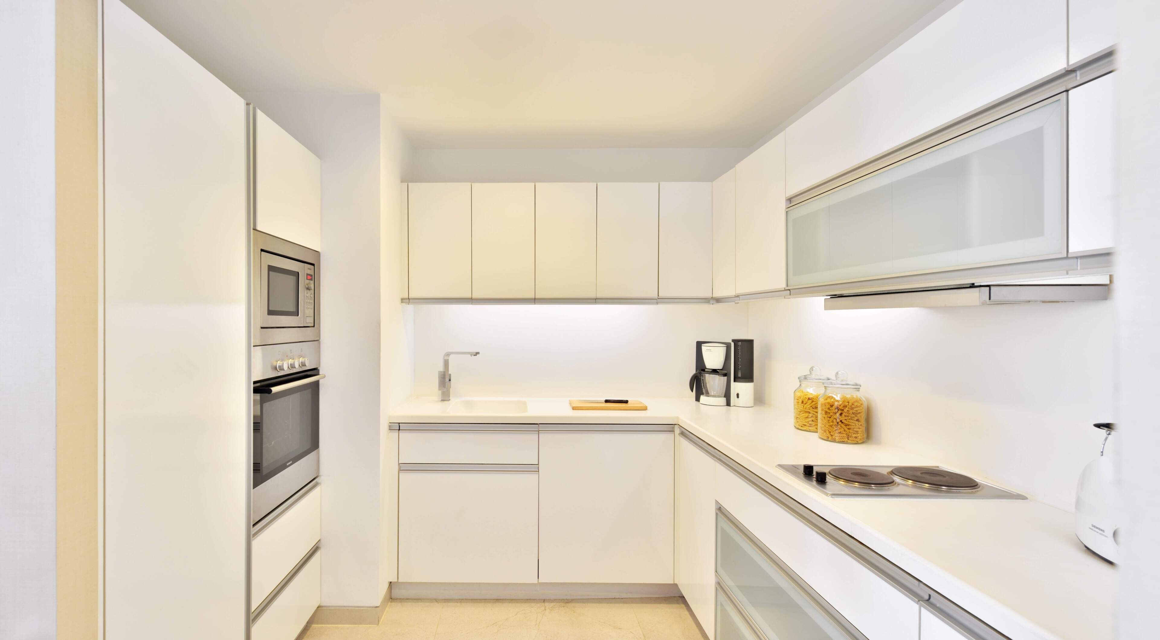 Una cocina moderna con armarios blancos, horno empotrado, microondas, cafetera y tostadora.
