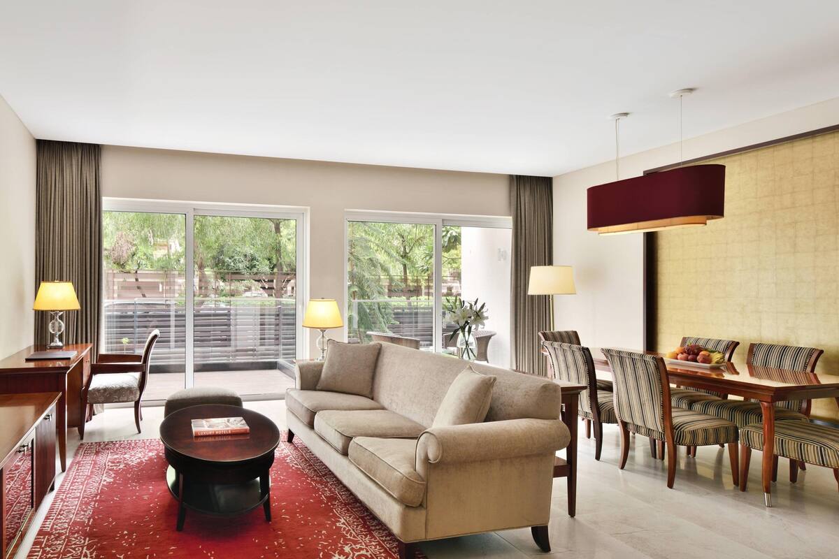 Ein modernes Wohnzimmer mit einer Couch, einem Couchtisch, einem Esstisch mit Stühlen und einem großen Fenster mit Blick auf Grünflächen.
