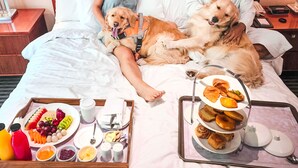 A hotel room with a tufted headboard, a bed with white linens, a tray of breakfast including fruits, pastries, and beverages, and a bedside table with a lamp and a clock. - Marriott Suites Pune (Pune)
