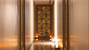 A corridor with reflective floors and walls, leading to a room with a patterned wall and candles on the side. - Marriott Suites Pune (Pune)