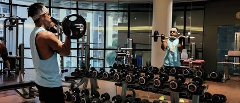 Un gimnasio con equipo de levantamiento de pesas y un espejo que refleja el interior.