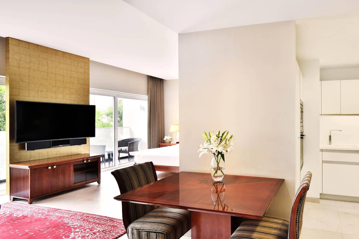 Ein modernes Hotelzimmer mit Essbereich, das einen Holztisch, gestreifte Stühle und eine Vase mit Blumen zeigt.