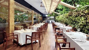 A restaurant with long wooden tables and chairs, glass walls, and a view of greenery. - Marriott Suites Pune (Pune)