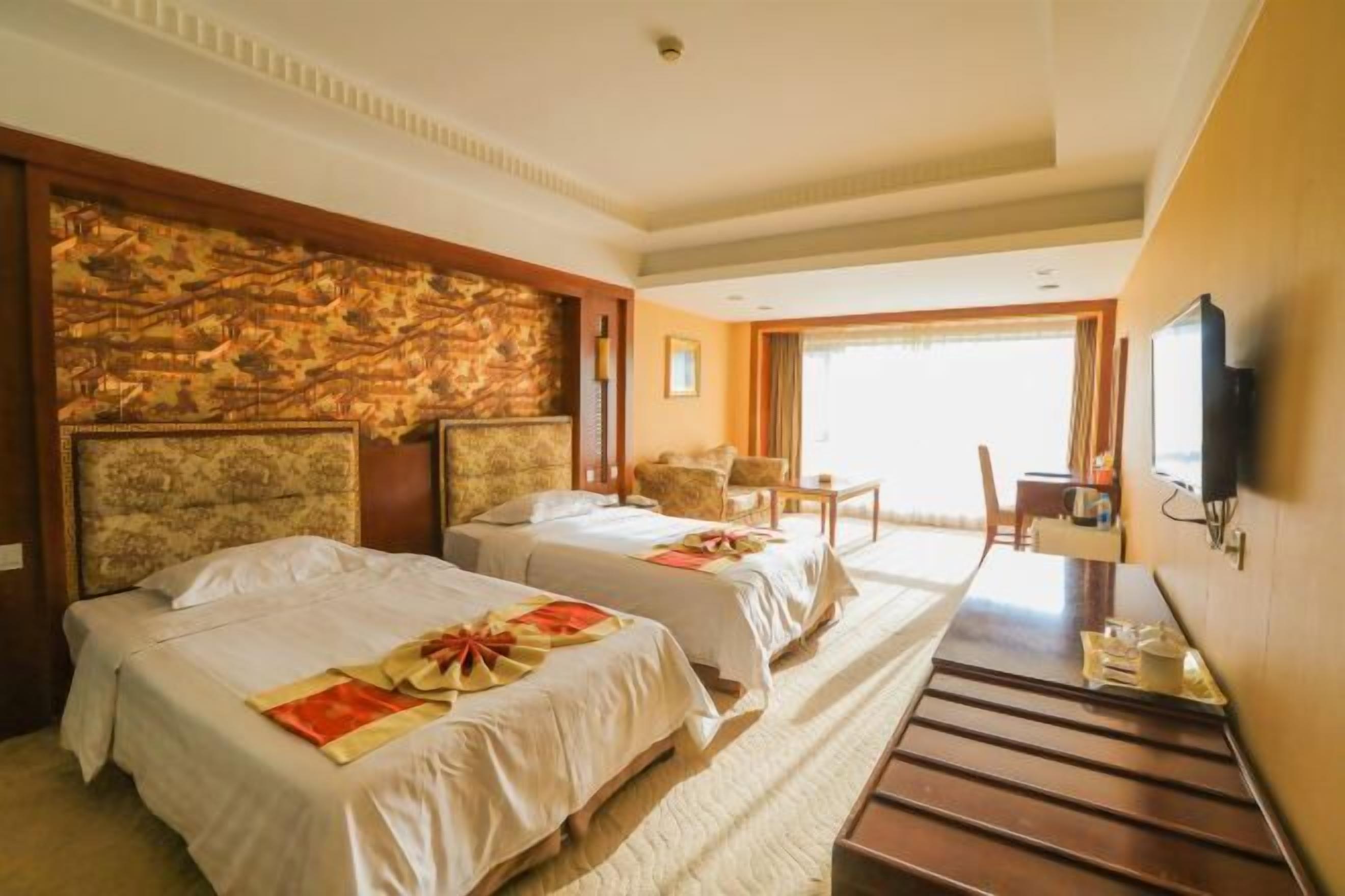 A hotel room with two beds, a stone accent wall, a television, and a view of the outdoors.