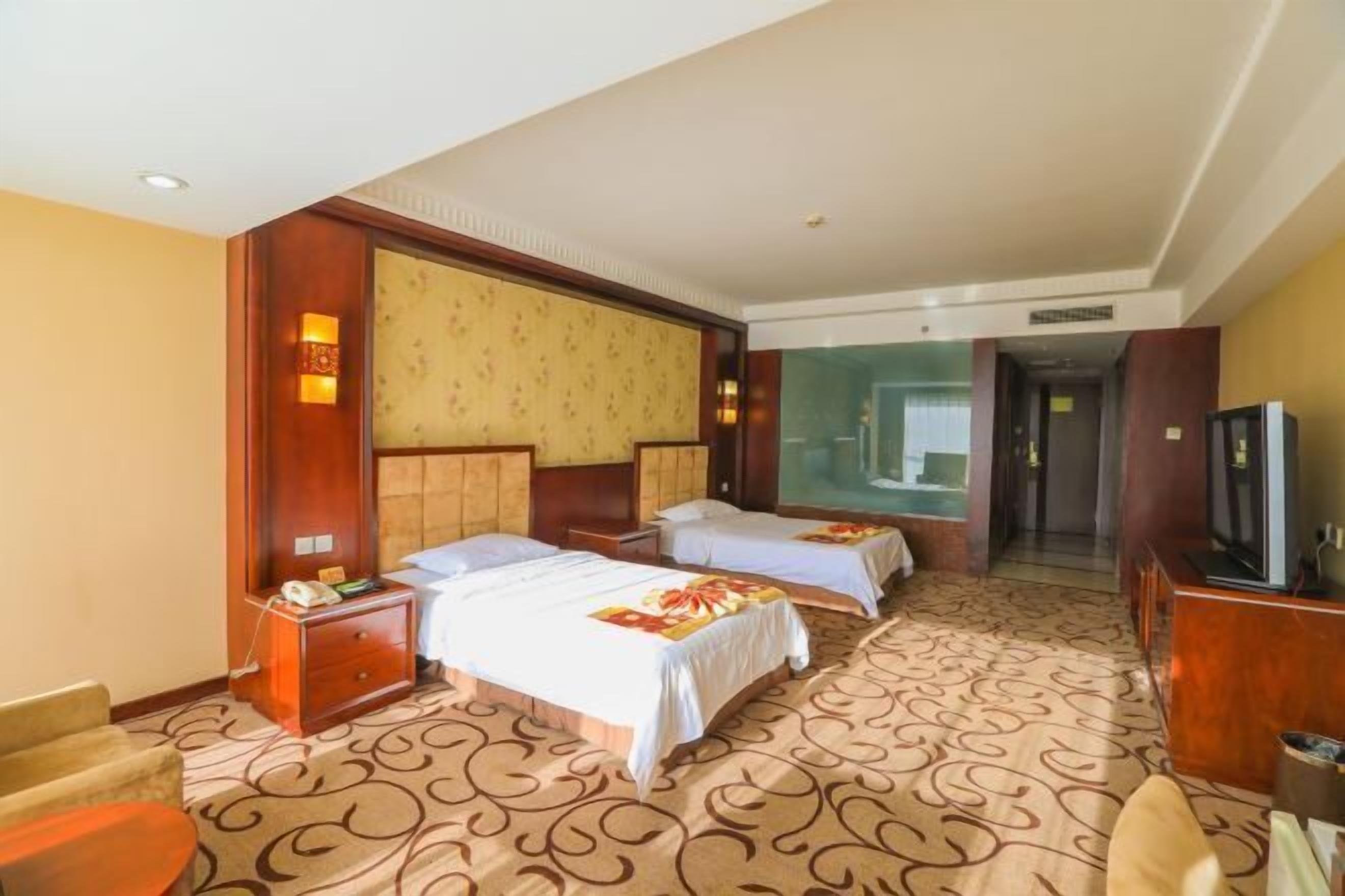 A hotel room with two beds, a TV, a desk, and a carpeted floor.
