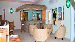 A room with wicker furniture, a bar area with bottles, and a large window with a view. - The Islander Hotel (Praslin Island)