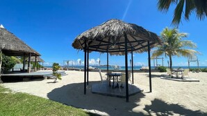 A beachside gazebo with a thatched roof, surrounded by palm trees and a sandy beach. - The Islander Hotel (Praslin Island)