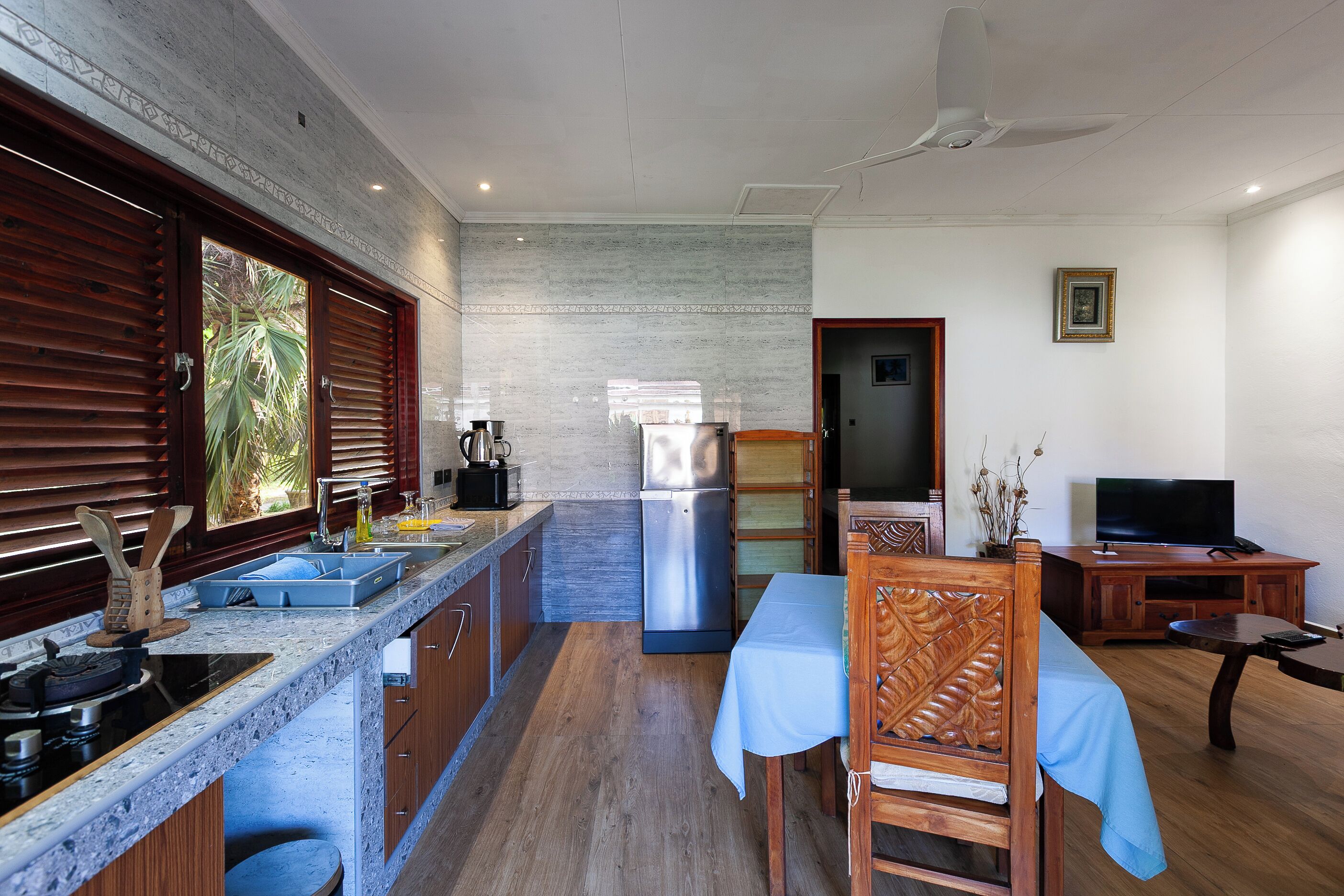 A modern kitchen with a built-in stove, sink, and refrigerator. There is a dining area with a table and chairs, and a television on a wooden cabinet.