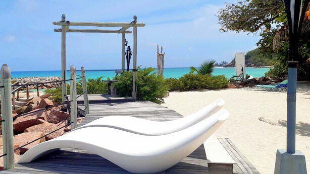 A beach walkway with a wooden structure and a white bench. - The Islander Hotel (Praslin Island)