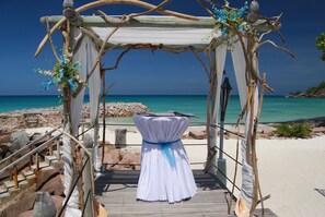 A wooden archway with a white draped canopy, leading to a beach with turquoise water. - The Islander Hotel (Praslin Island)