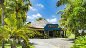 A restaurant with a thatched roof, surrounded by palm trees and greenery. - The Islander Hotel (Praslin Island)