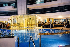 An indoor pool area with a glass barrier, surrounded by tables and chairs, and a festive decoration with lights and ornaments.