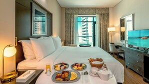 A hotel room with a bed, breakfast tray, bedside table, lamp, and a view of a building and water. - TIME Oak Hotel & Suites (Dubai)