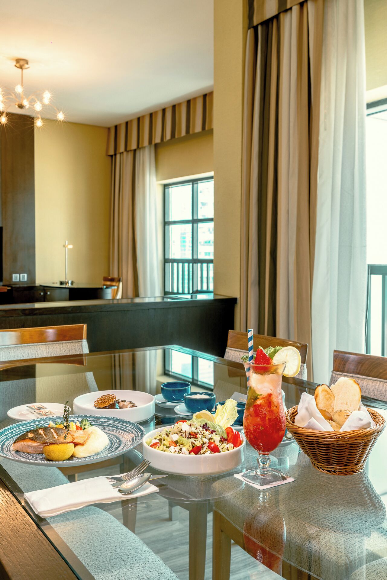 A dining table with plates of food, a glass of drink, and a basket of bread.