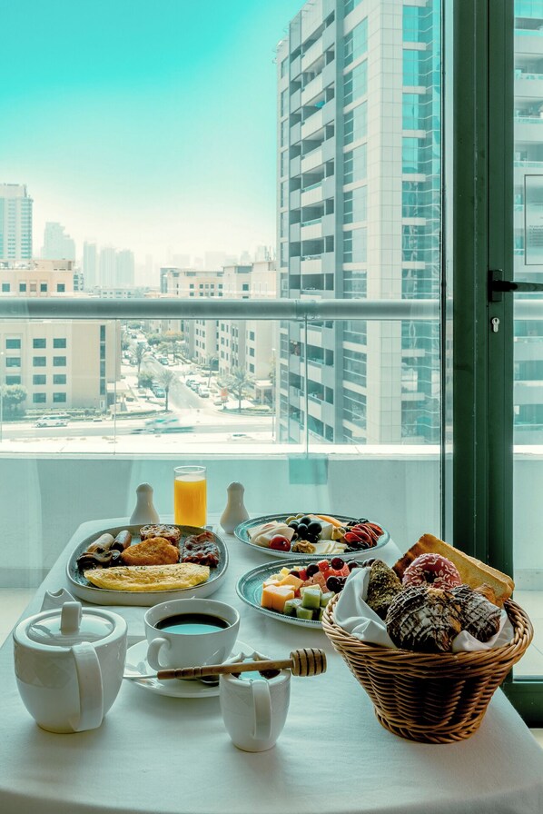 A breakfast setup with various dishes and drinks on a balcony with a city view.