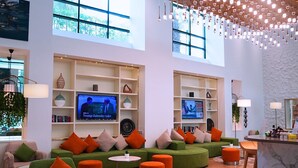 A modern lounge area with green sofas, orange cushions, and a TV displaying news. - TIME Oak Hotel & Suites (Dubai)