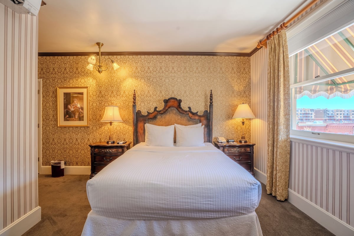 A hotel room with a large bed, two bedside tables with lamps, a framed picture on the wall, and a window with curtains.