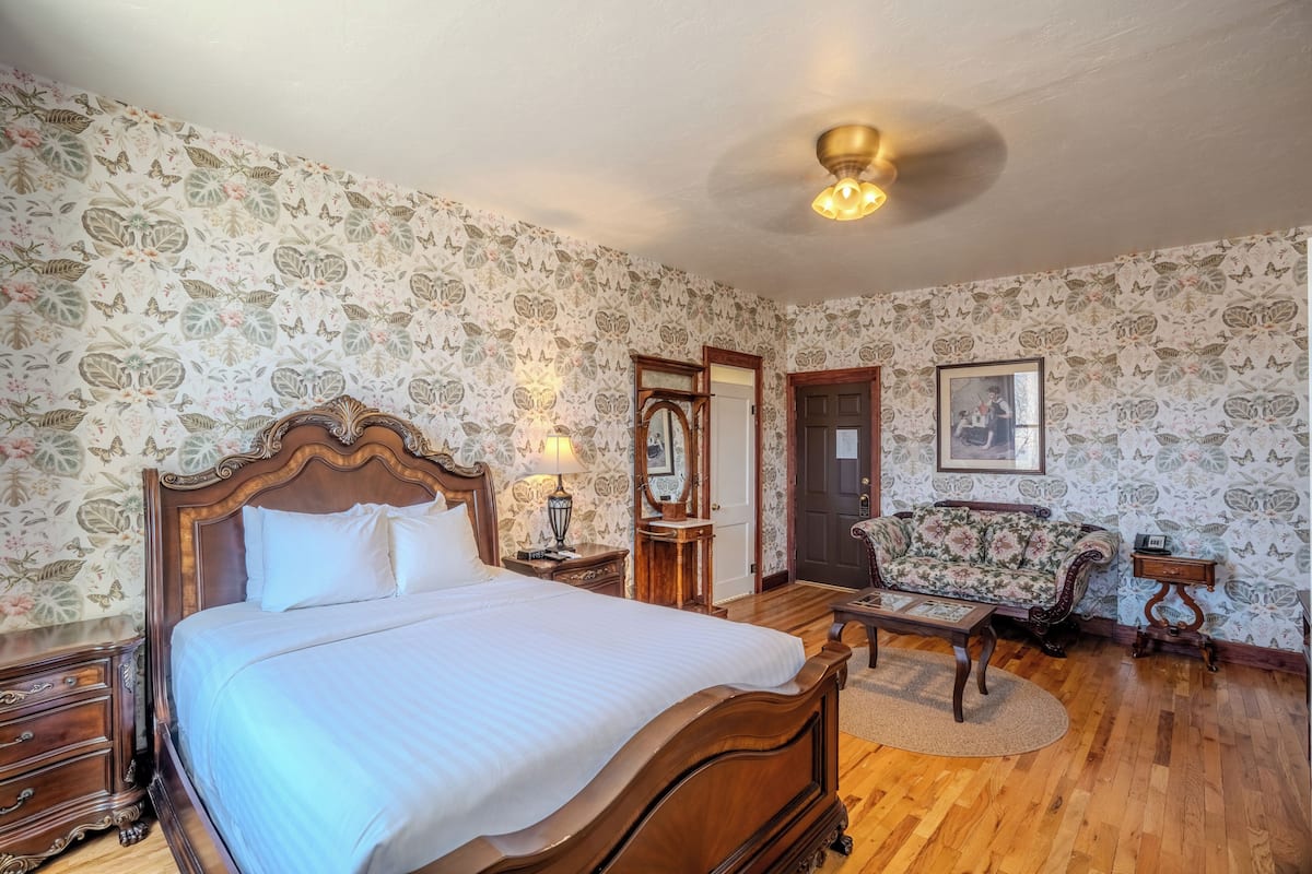 A bedroom with a wooden bed, a nightstand, a dresser, a floral sofa, and a ceiling fan.