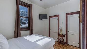 A bedroom with a bed, a ceiling fan, a TV mounted on the wall, and two doors.