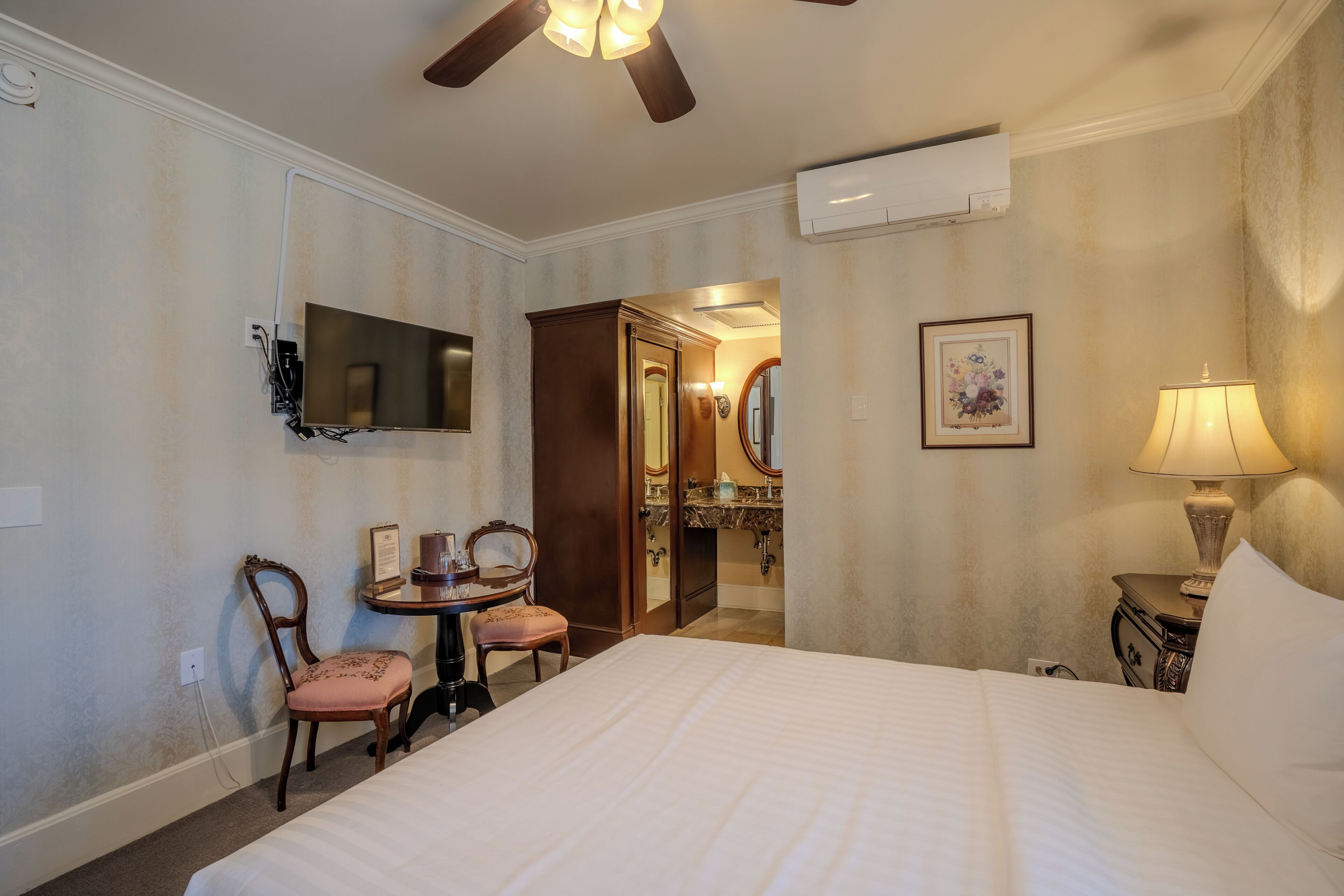 Une chambre d’hôtel comprenant un lit, un bureau avec une chaise, une télévision, un miroir, une lampe et un appareil de climatisation.
