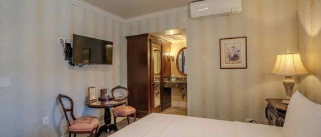 Une chambre d’hôtel comprenant un lit, un bureau avec une chaise, une télévision, un miroir, une lampe et un appareil de climatisation.