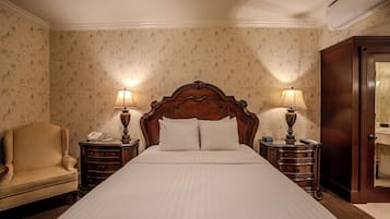 Une chambre d’hôtel avec un grand lit, deux tables de chevet avec des lampes, une tête de lit en bois, une armoire en bois et une chaise.