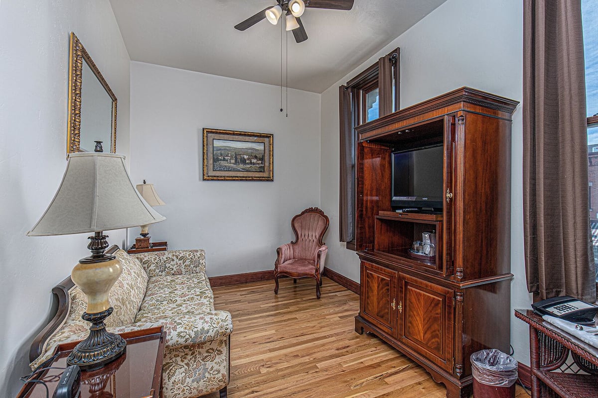 A living room with a wooden floor, a sofa, a chair, a cabinet with a television, and a ceiling fan.
