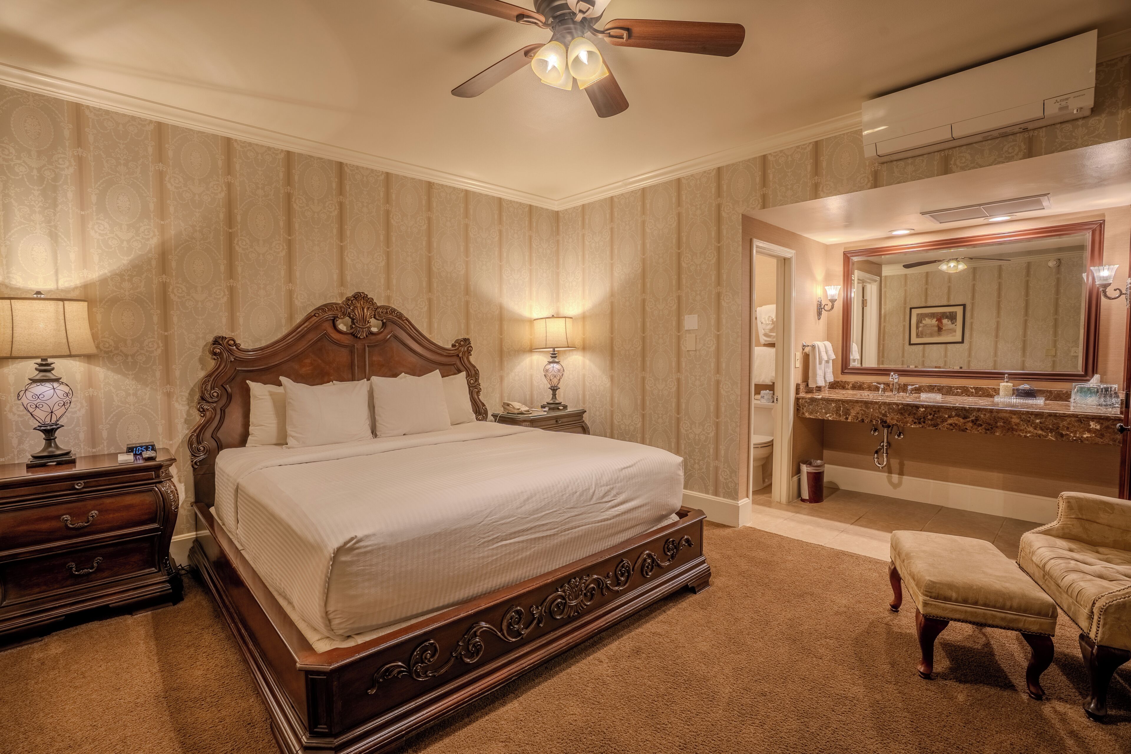 A bedroom with a large bed, a ceiling fan, a vanity with a mirror, and a chair.