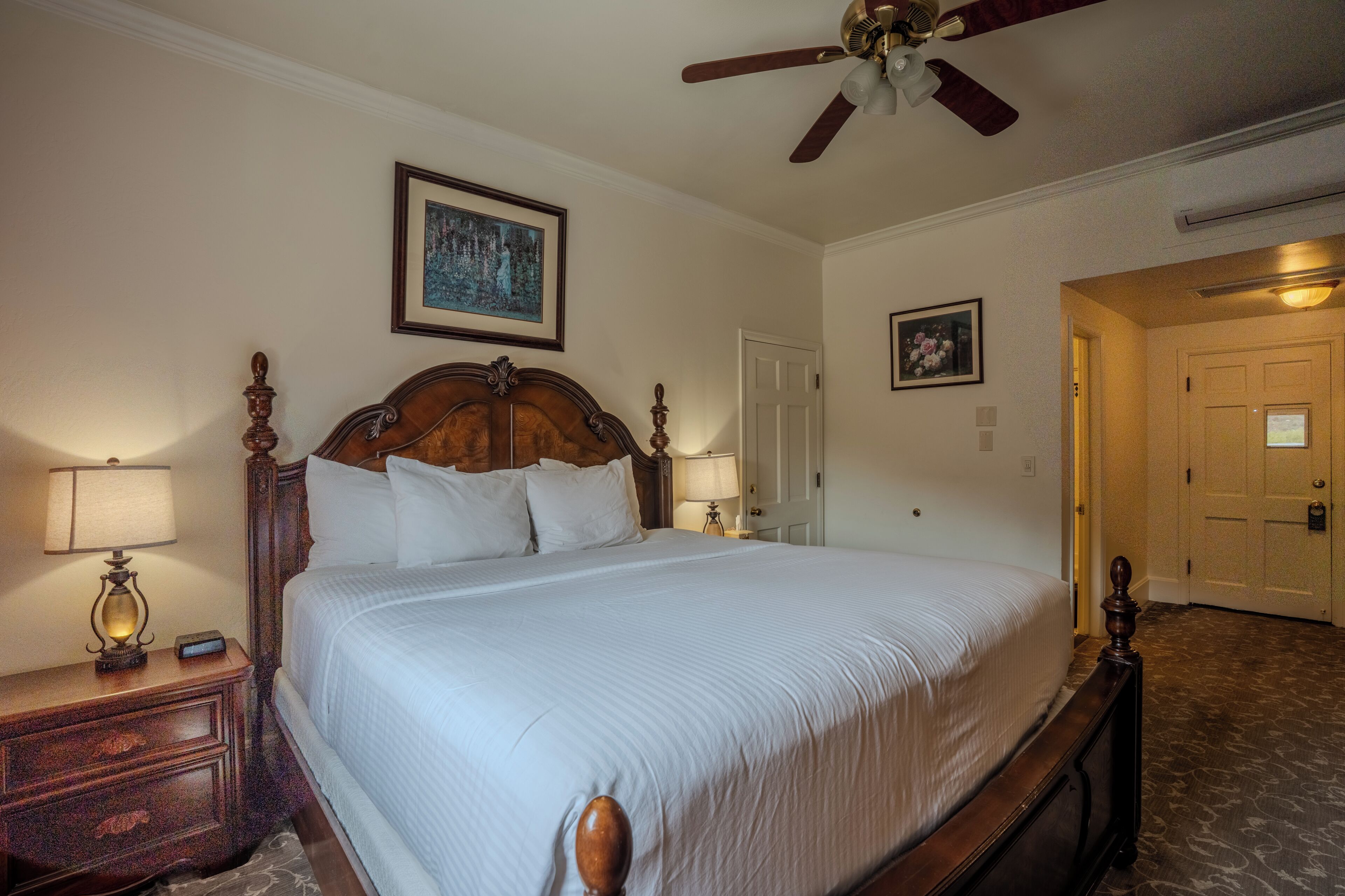 A neatly made bed with a wooden headboard, two bedside lamps, a ceiling fan, and a framed picture on the wall.