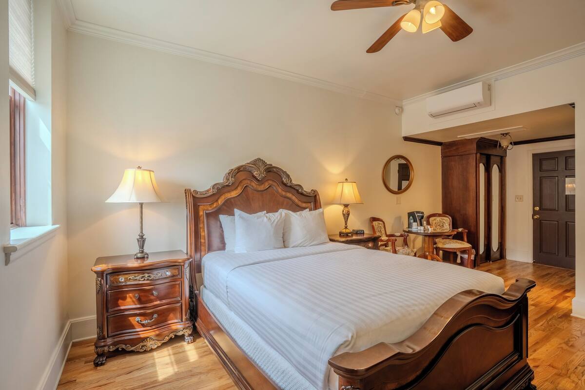 A bedroom with a wooden bed, two bedside tables with lamps, a mirror, and a door.