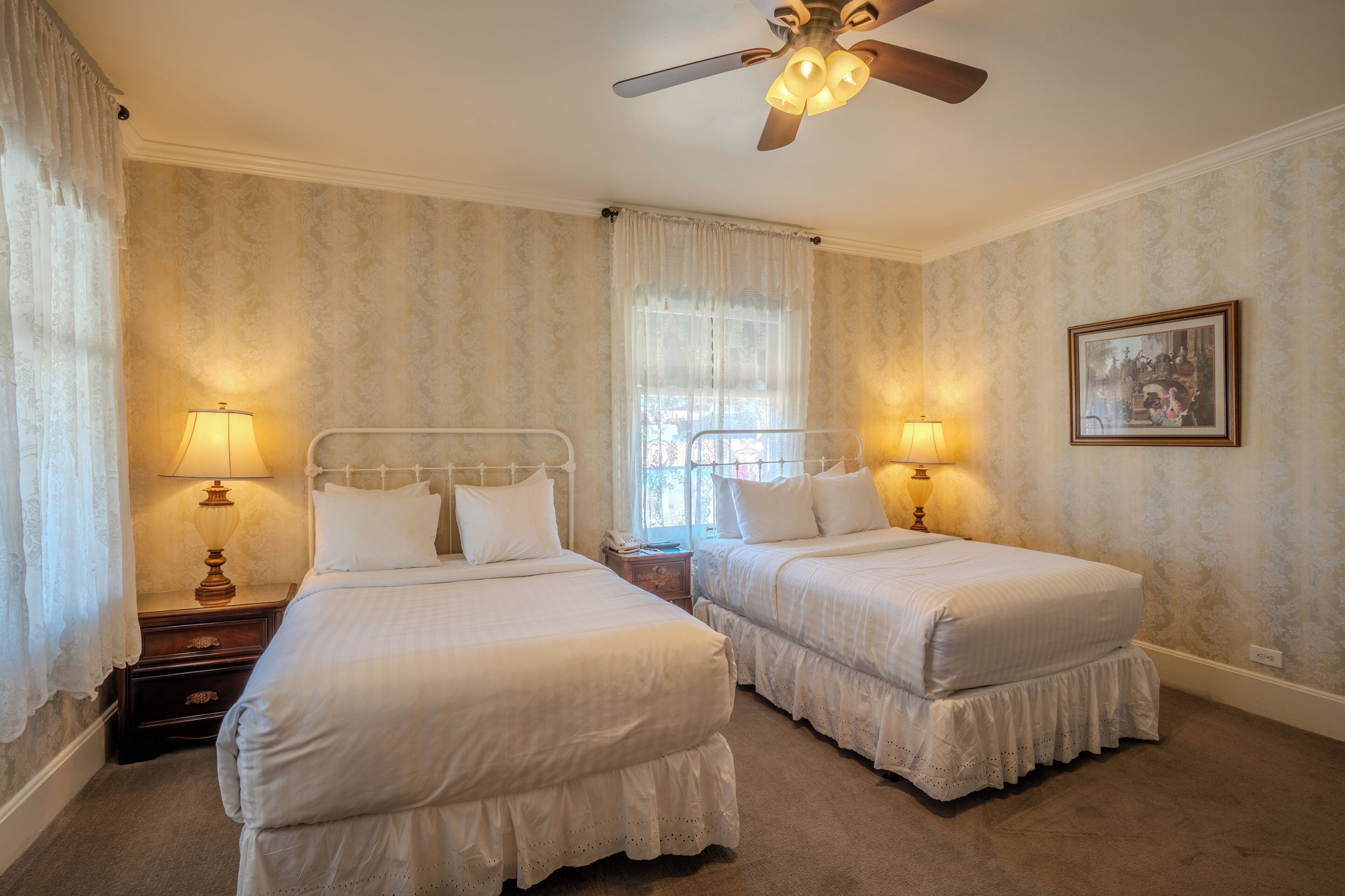 A room with two beds, a ceiling fan, and a window with curtains.