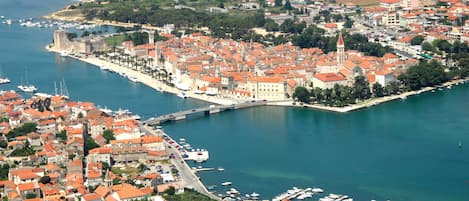 An aerial view of a coastal town with a prominent castle, marina, and densely packed red-roofed buildings.