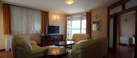 A living room with two sofas, a coffee table, a TV, and a large window with curtains.