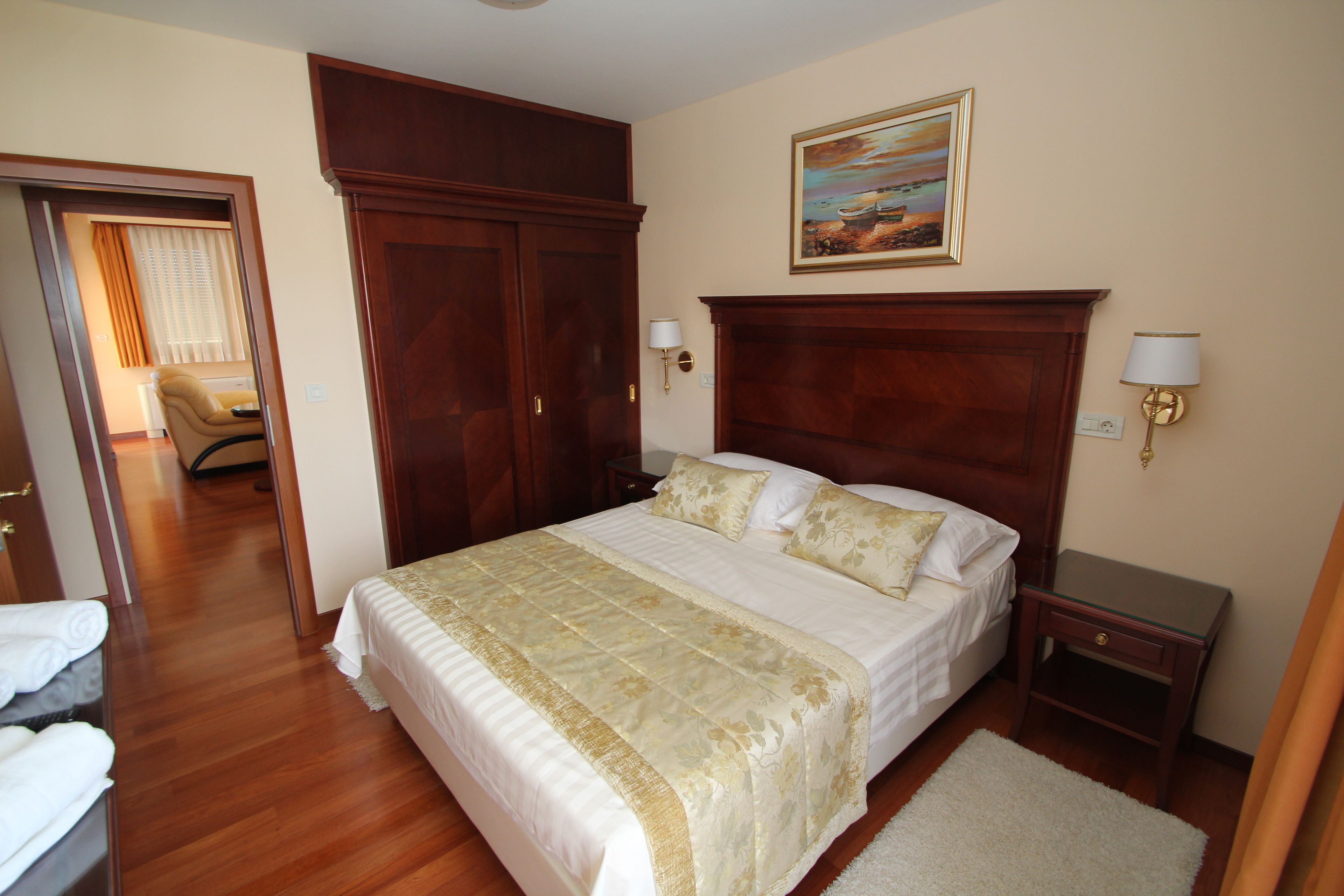 A neatly arranged bedroom with a large bed, wooden wardrobe, and a painting on the wall.
