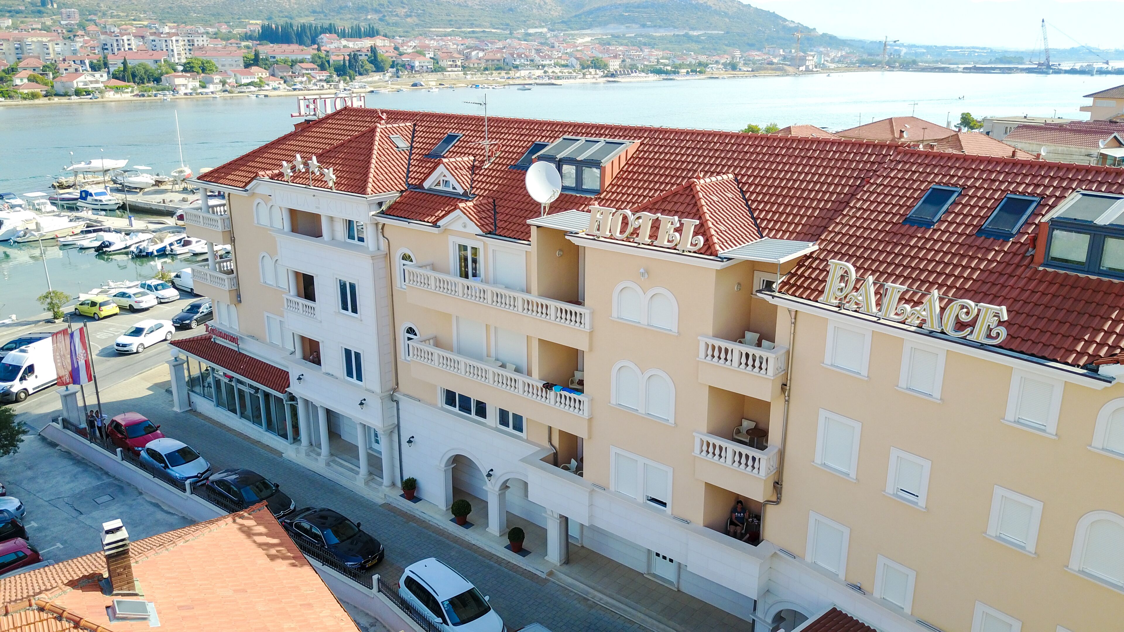 Ein mehrstöckiges Hotel mit Balkonen, im Hintergrund ein Yachthafen und Blick auf das Wasser.