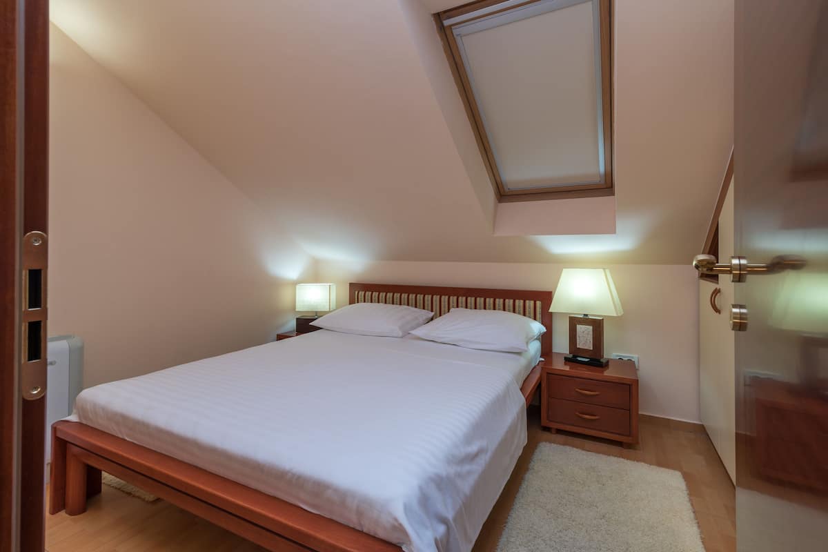 A bedroom with a bed, bedside tables, lamps, and a wooden headboard.