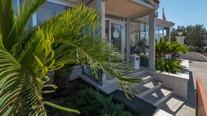 A modern building with a glass entrance, a palm tree in the foreground, and a clear sky. - Hotel Trogir Palace (Trogir)