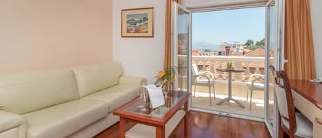 A living room with a sofa, a glass-top coffee table, a painting on the wall, and a view of a balcony with outdoor furniture.