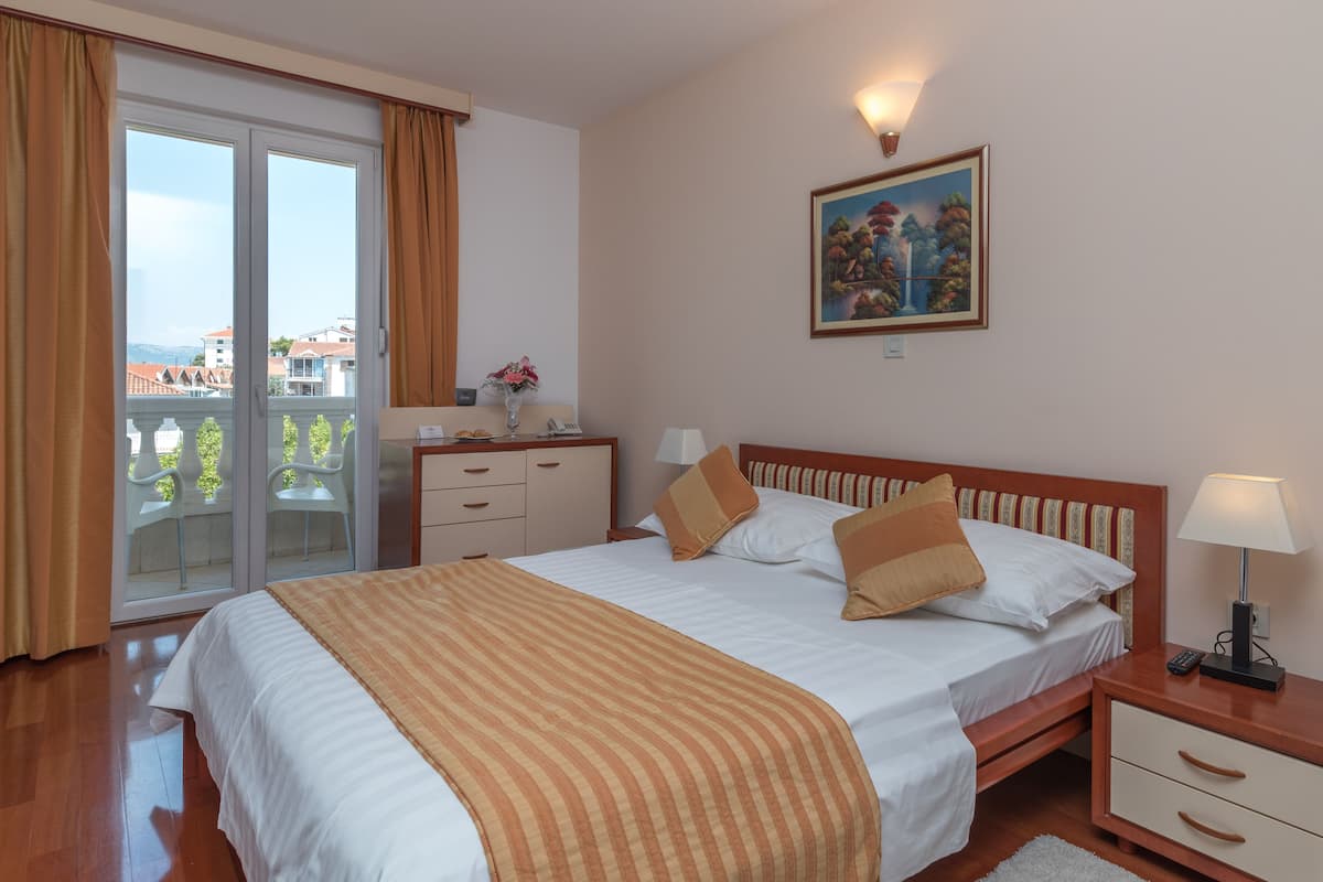A hotel room with a bed, a desk, a chair, a nightstand, a lamp, and a painting on the wall.