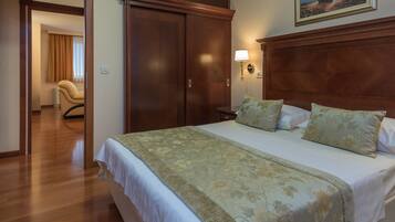 A hotel room with a large bed, wooden wardrobe, and a chair.