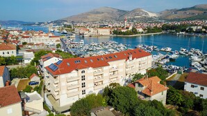 A coastal town with a marina filled with boats, a prominent building with a red roof, and a mountainous backdrop. - Hotel Trogir Palace (Trogir)