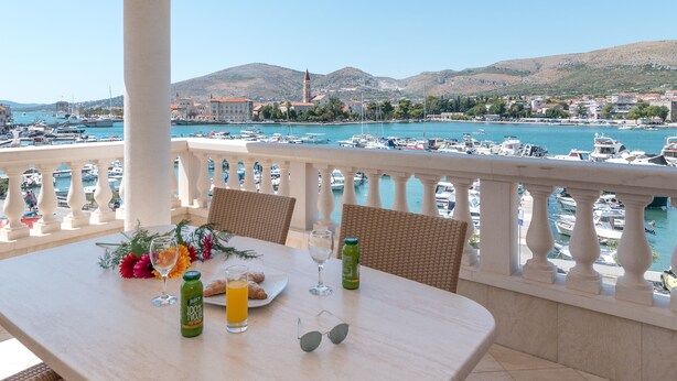A balcony with a table set for breakfast, overlooking a marina with boats and a mountainous backdrop. - Hotel Trogir Palace (Trogir)